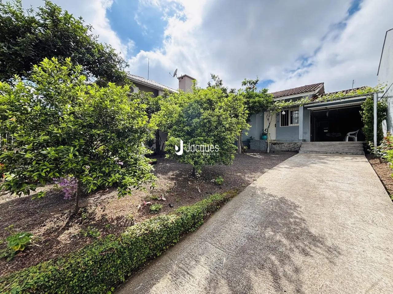 Vista da fachada de uma residência com jardim e entrada pavimentada.