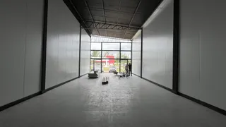Vista interna de um espaço amplo com paredes brancas e teto industrial.