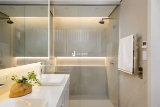 Interior de um banheiro moderno com bancada branca e box de vidro.