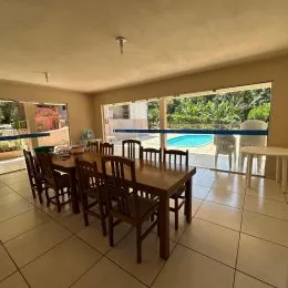 Sala de jantar com mesa de madeira e janelas amplas na área interna.