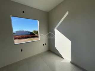 Vista de uma janela mostrando um terreno seco e um prédio branco ao fundo.
