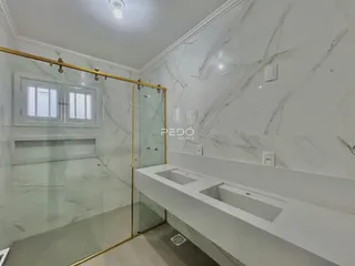 Banheiro com revestimento em mármore e box de vidro.