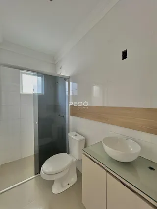 Interior de um banheiro com revestimento cerâmico e box de vidro.