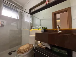 Foto de um banheiro com box de vidro e bancada de granito marrom.
