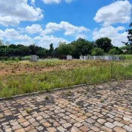 Área externa pavimentada com tijolos em um terreno com vegetação rasteira.