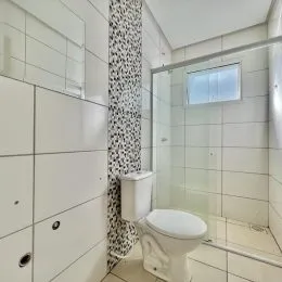 Banheiro com revestimento de azulejos brancos e box de vidro.