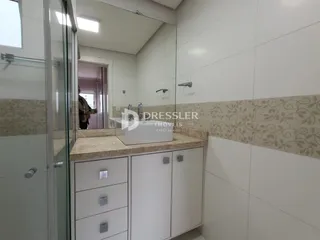 Banheiro com box de vidro e armários brancos.