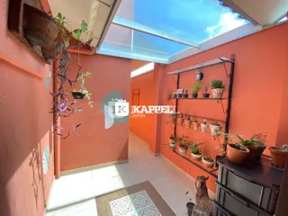 Vista interna de um corredor com paredes cor de terracota e iluminação natural de um teto de vidro.