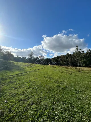 Campo gramado aberto sob um céu azul com nuvens.
