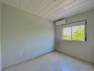 Esta é uma sala interna com paredes brancas e piso de porcelanato, com ar-condicionado e janela.