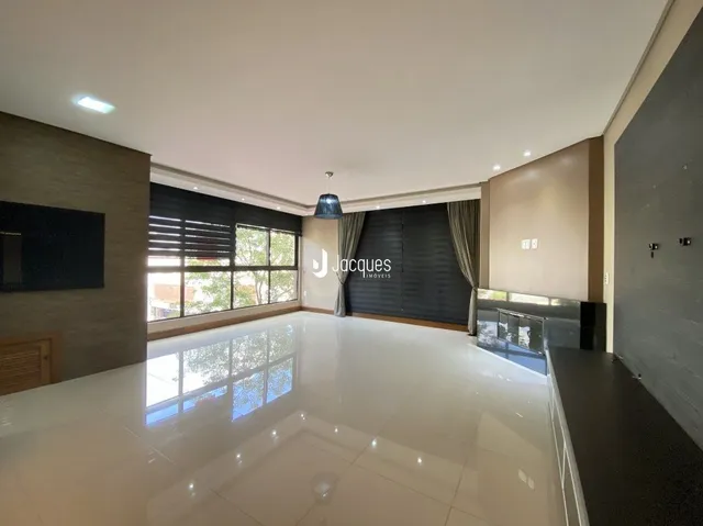 Ambiente interno de uma sala ampla com piso claro e grandes janelas.