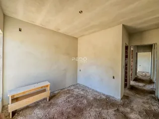 A foto mostra um cômodo interno em estado de obra com paredes brancas e piso de terra.