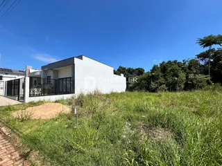Fachada de uma casa branca com jardim gramado e vegetação densa ao fundo.