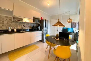 Ambiente de cozinha e jantar aberto com armários brancos e mesa de jantar amarela.
