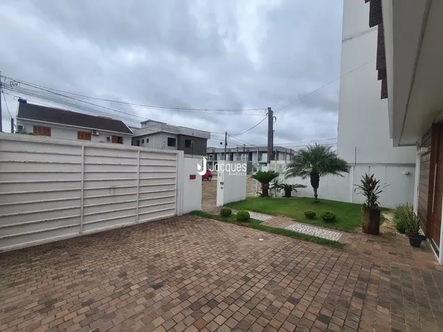 Vista externa de uma propriedade com muro branco e área pavimentada.