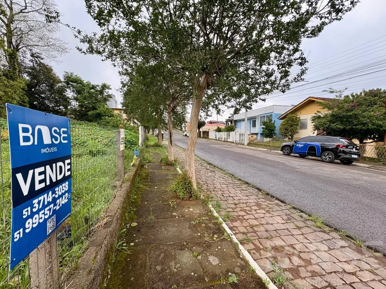 Vista de uma rua em Lajeado, Brasil, com uma placa de anúncio de imobiliária.