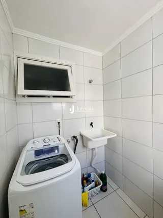 Foto de um banheiro com revestimento cerâmico branco e máquina de lavar roupa.