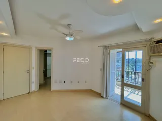 Ambiente interno de uma sala ampla com piso de madeira clara e porta de vidro abrindo para a varanda.