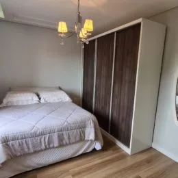 Quarto com cama de casal e piso de madeira clara.