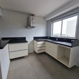 Foto interna de uma cozinha com armários brancos e bancadas escuras.