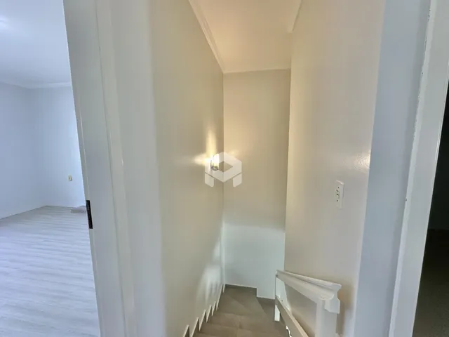 Hall da casa com piso de madeira e paredes brancas.