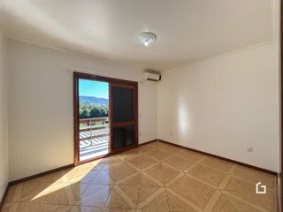 Interior de uma sala com piso de madeira clara e porta de vidro com vista para a paisagem.