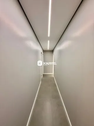 Corredor longo e estreito com paredes brancas e iluminação embutida.