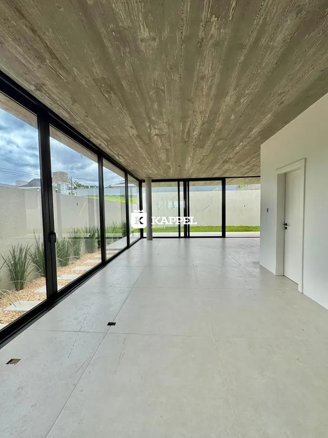 Vista interna de um espaço amplo com piso de concreto e grandes portas de vidro.
