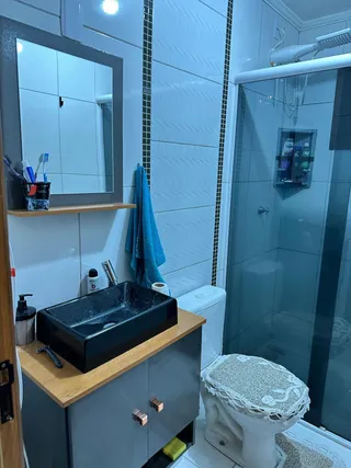 Foto de um banheiro com pia escura e box de vidro transparente.