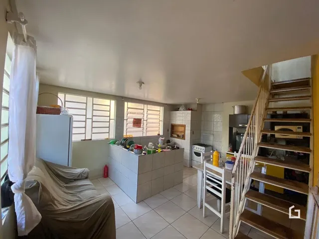 Vista interna de uma sala de estar com cozinha e escadaria em um imóvel no Brasil.