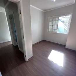 Vista interna de um cômodo com piso de madeira e paredes brancas.