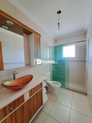 Banheiro com bancada de madeira e box de vidro transparente.