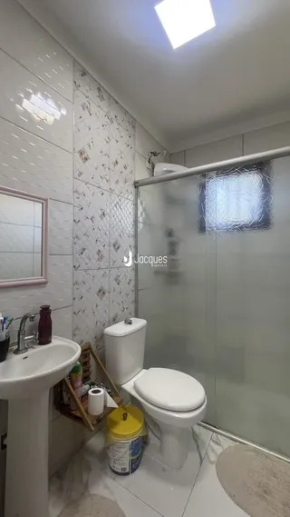 Interior de um banheiro com azulejos brancos e louças sanitárias brancas.