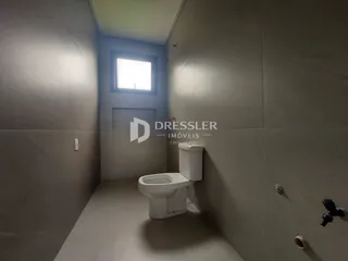 Foto de um corredor interno mostrando um vaso sanitário branco e uma janela.