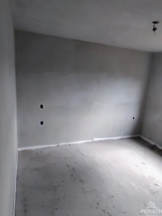 Foto de um cômodo interno vazio com paredes brancas e piso cru.