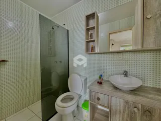Banheiro com revestimento cerâmico e box de vidro.