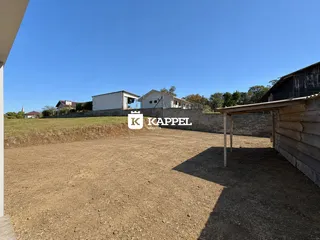 Vista de uma área externa de terra batida com construções ao fundo.