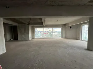 Vista interna de um espaço amplo com piso de concreto aparente e paredes brancas.