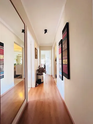 Corredor interno de uma residência com piso de madeira clara.