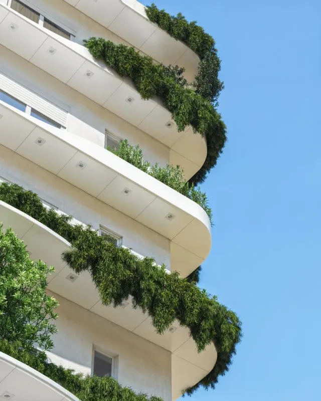 Fachada de um prédio residencial com varandas cobertas por vegetação verde.
