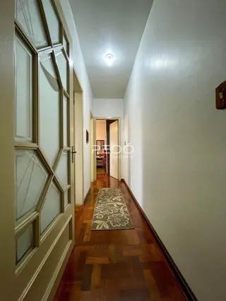 Corredor interno de uma residência com piso de madeira e parede clara.