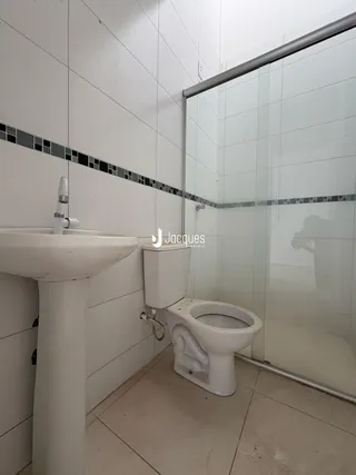 Imagem de um banheiro com revestimento cerâmico branco e box de vidro.