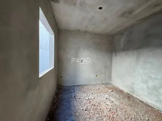 Foto de um cômodo interno com paredes de concreto e piso de terra.