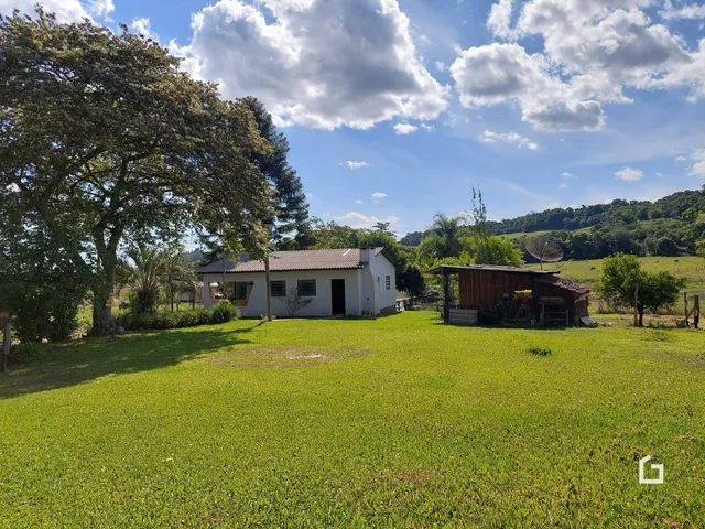 Vista externa de uma casa rural com gramado e campo verde.