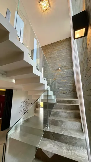 Hall de entrada com escadaria e guarda-corpo de vidro em um imóvel.