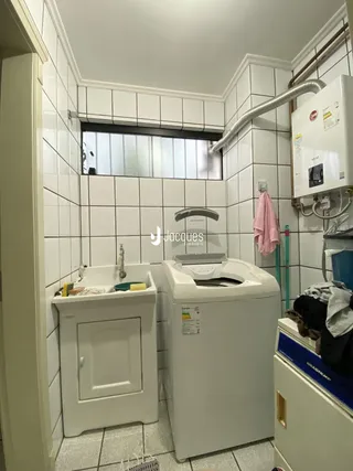 Interior de um banheiro com azulejos brancos e máquina de lavar roupa.