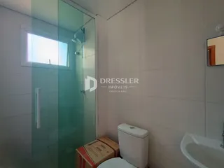 Vista interna de um banheiro com box de vidro e vaso sanitário.