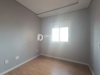 Vista interna de um cômodo com paredes brancas e piso de madeira clara.