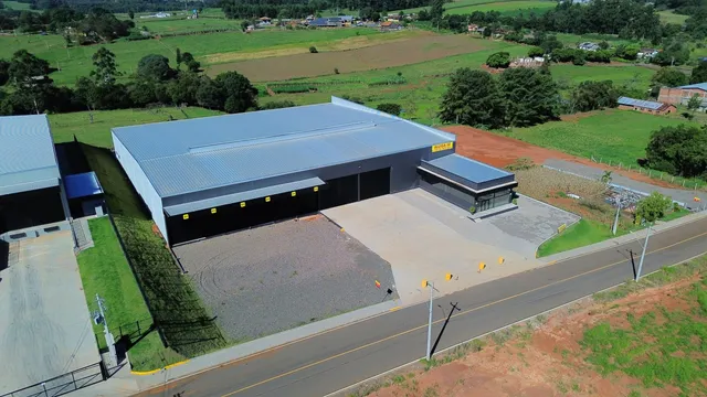 Fachada de um grande galpão industrial em uma área rural.