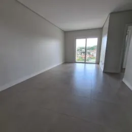 Sala de estar ampla com paredes brancas e piso claro, mostrando um espaço vazio.